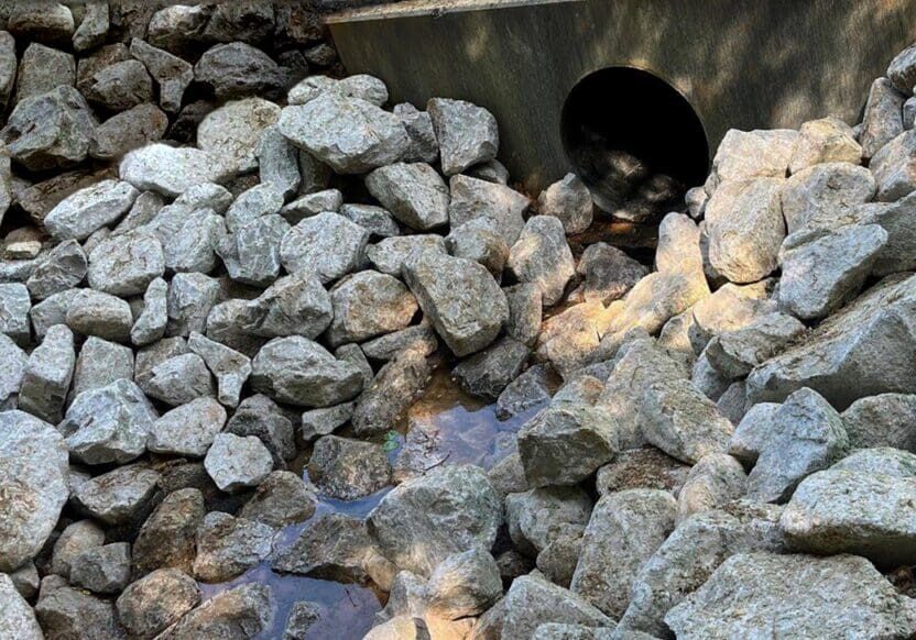 Pile of gray rocks beside a drainage pipe outdoors.