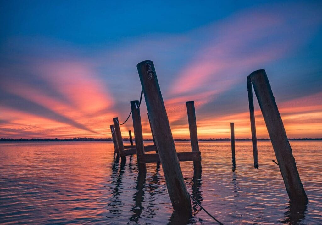 Sunset over a calm water body with wooden posts.