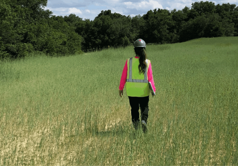 A person hiking in a green field under a partly cloudy sky.