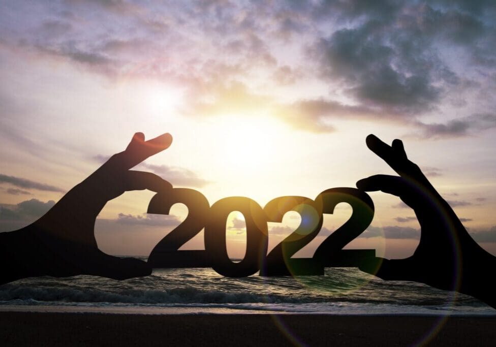Silhouettes holding '2022' against a sunset sky over the ocean.
