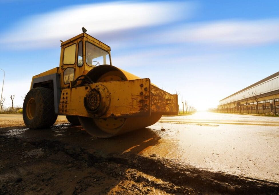 Yellow road roller working on a dirt road at sunrise.