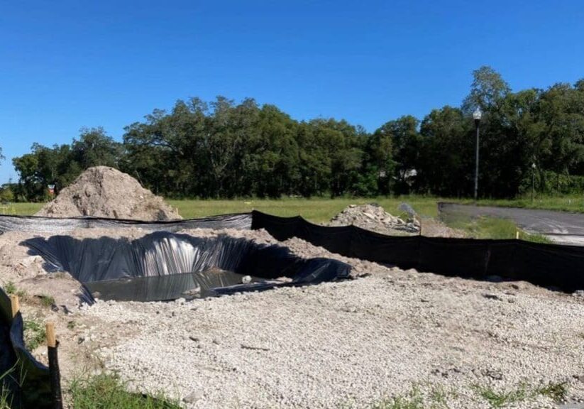 Large sinkhole with water and debris in a gravel area near trees.