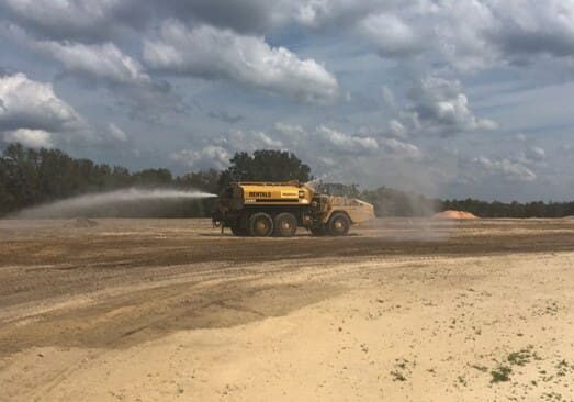A yellow bulldozer working on a sandy construction site under a cloudy sky.