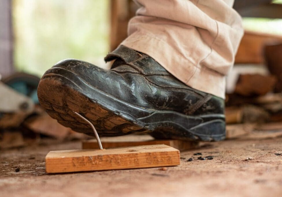 A boot stepping on a wooden mousetrap outdoors.