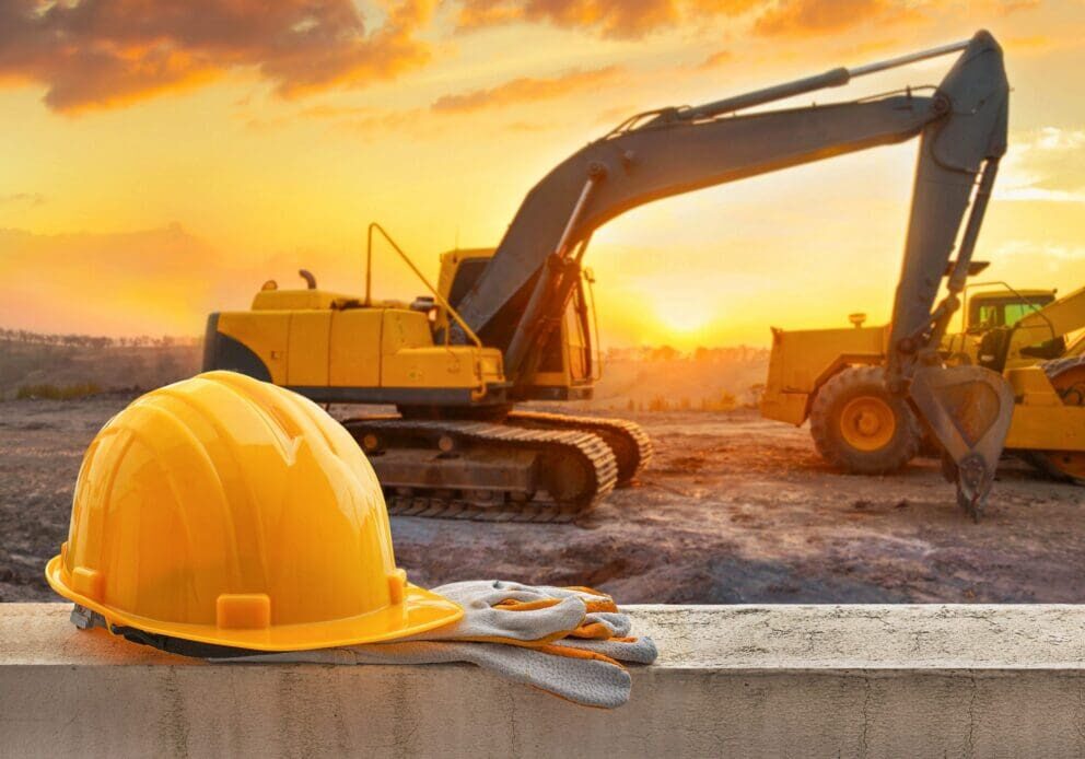 Construction site with excavator and safety helmet at sunset.